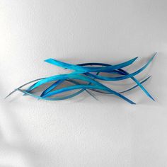 a blue sculpture is hanging on the wall in front of a white wall and it looks like an abstract piece of art