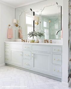 a white bathroom with gold accents and marble counter tops is pictured in this image, there are two mirrors above the double sinks