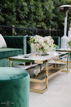 a living room with green velvet couches and white flowers in vases on the coffee table