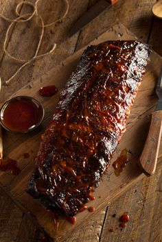 a large piece of meat sitting on top of a wooden cutting board next to sauce