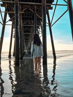 a woman standing under a pier looking at the water