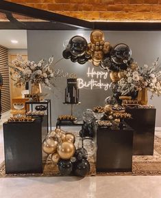 black and gold balloons are on display in front of a happy birthday sign with white flowers