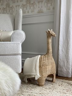 a giraffe statue sitting next to a white chair in a room with wallpaper