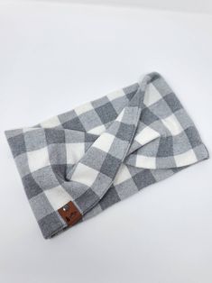 a gray and white checkered scarf laying on top of a white tablecloth with a brown leather tag