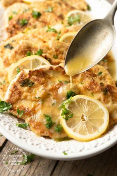 a white plate topped with chicken covered in sauce and lemon slices next to a spoon