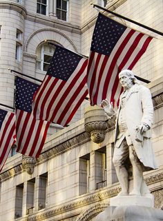 several american flags flying in the wind next to a building with a statue on it