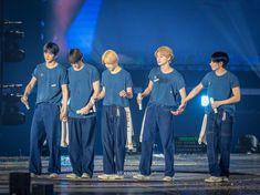 group of young men standing on stage with microphones in their hands and wearing blue t - shirts