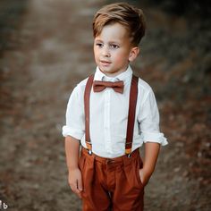 a young boy wearing brown suspenders and a bow tie standing in the middle of a dirt road