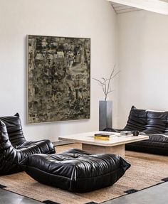 a living room with black leather furniture and a large painting on the wall behind it