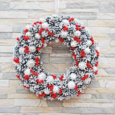 a wreath hanging on the side of a brick wall with red berries and pine cones