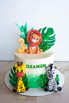 a three tiered cake decorated with animals and palm leaves on the top, along with number 3