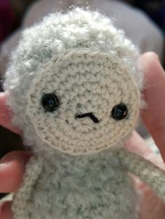 a hand holding a small white crocheted teddy bear with black eyes and nose