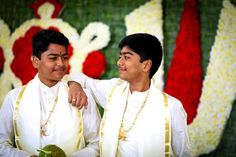 two men standing next to each other in front of a wall with flowers on it