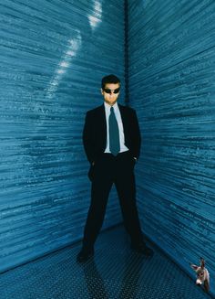 a man in a suit and sunglasses standing next to a wall with a cat on the floor