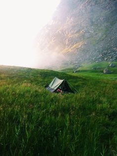 a tent pitched up in the grass with mountains in the background