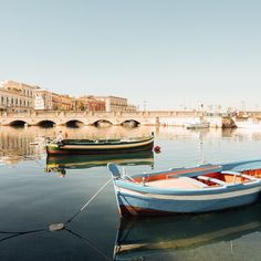 two boats are tied up in the water near a bridge and buildings on either side