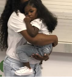 a woman holding a small child in her arms while standing next to a white wall