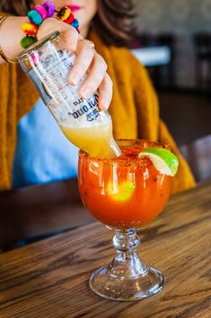 a woman pouring a drink into a glass on top of a wooden table next to a bar