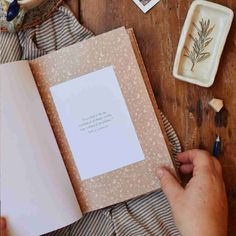 someone is holding an open book on a table with other items and writing utensils