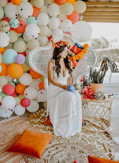 a woman in a white dress sitting on a wicker chair with balloons behind her