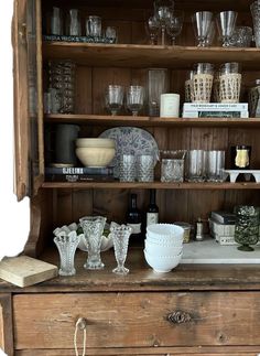 an old wooden hutch filled with glasses and other items on top of it's shelves