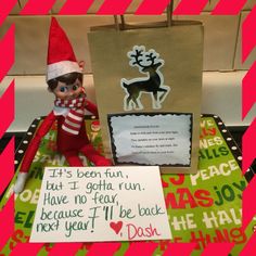 an elf is sitting next to a bag with a note on it and a christmas card