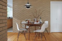 a dining room table with four chairs next to a brick wall and wooden flooring