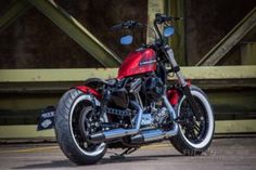 a red motorcycle parked on top of a parking lot next to a metal bridge overpass