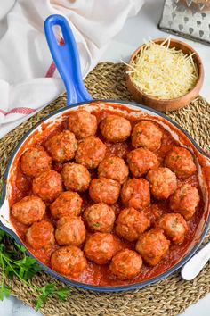 meatballs in marinara sauce with parmesan cheese on the side and blue serving spoon