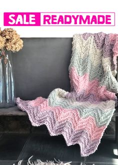 a pink and white crocheted blanket sitting on top of a wooden bench next to a vase with flowers