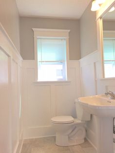 a white toilet sitting next to a sink in a bathroom under a window with blinds