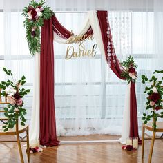 the wedding arch is decorated with red and white draping, greenery and flowers