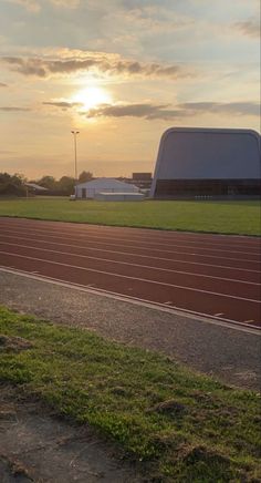 the sun is setting over a track with grass and dirt in front of it,