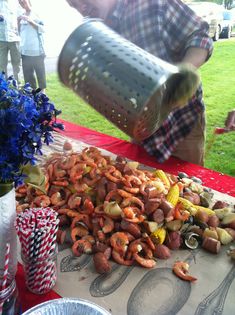 a man pouring corn on the cob into a pile of hot dogs and potatoes