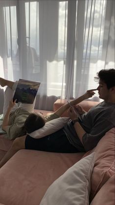 two people are laying on a couch reading books while one person is lying down with his feet up