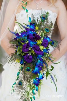 a bride holding a purple and green bouquet with peacock feathers on it's side