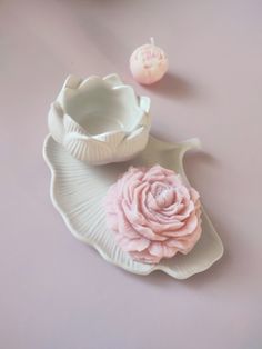 a pink flower sitting on top of a white plate next to an empty cupcake