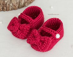 a pair of red knitted baby shoes sitting on top of a white blanket next to a tree