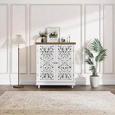 a white cabinet sitting on top of a wooden floor next to a potted plant