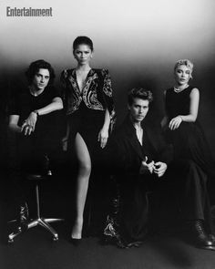 four people are posing for a black and white photo with one person leaning on the chair