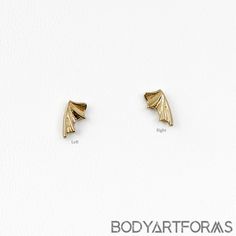 two small gold earrings on top of a white surface with the words body artforas written