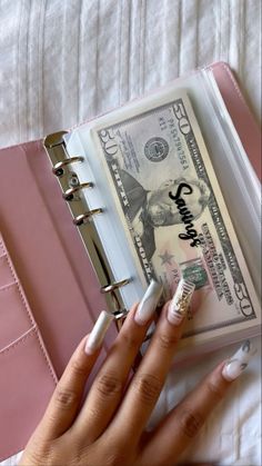 a woman's hand holding a pink binder with money in it and a note book