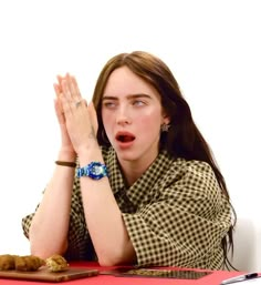 a woman sitting at a table with her hands up to her face and looking surprised