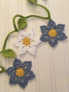 three crocheted flowers are hanging on a white wall with green stems and leaves