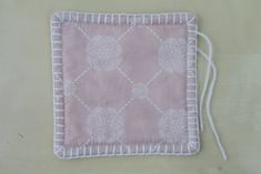 a pink and white square shaped object with tassels on the sides, sitting on a table