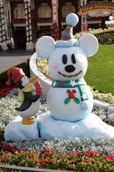 mickey mouse and penguin snowman statue in front of the disneyland world christmas village entrance