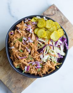 a bowl filled with coleslaw and pickles on top of a cutting board