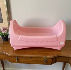 a pink baby bath tub sitting on top of a wooden table next to a potted plant