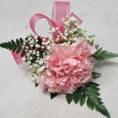 a pink carnation and baby's breath flower corsage with ribbon tied around it