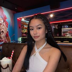 a woman sitting at a table with a drink in front of her and a movie poster behind her